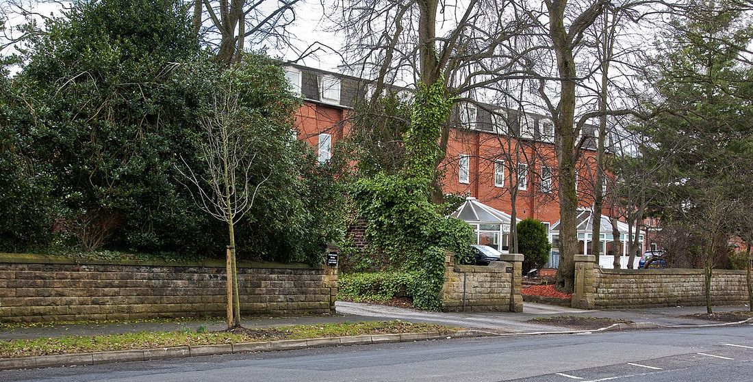 A brick nursing home set back behind a garden wall